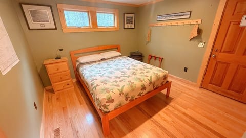 Comfortable queen bedroom with warm wood flooring, natural light, and a peaceful setting perfect for a relaxing cabin getaway.