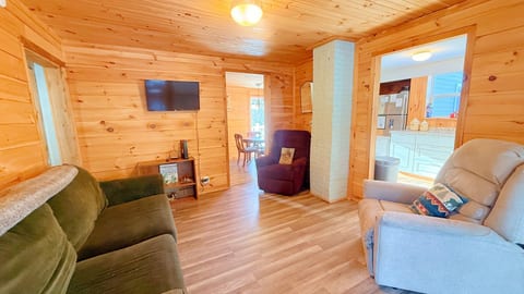 Cozy wood-paneled living room with comfortable seating, a TV, and warm cabin charm.