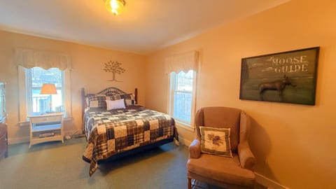 Cozy queen bedroom with rustic décor, natural light, and a comfortable reading chair.