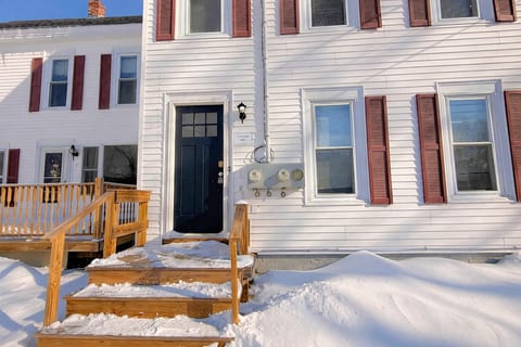 Charming downtown townhouse with a welcoming front entry, classic shutters, and fresh snowfall.