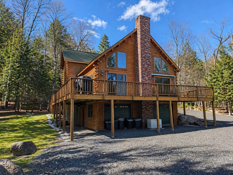 Spacious log cabin with a wraparound deck, towering fireplace, and peaceful wooded surroundings.