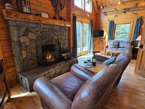 Rustic log cabin living room with a stone fireplace, soaring ceilings, and cozy woodland charm.