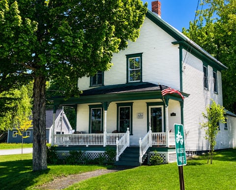 Charming white farmhouse retreat with a wraparound porch, shaded yard, and peaceful small-town setting.