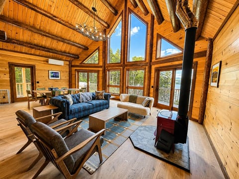 Spacious log cabin living room with vaulted ceilings, a wood stove, and large windows overlooking the water.