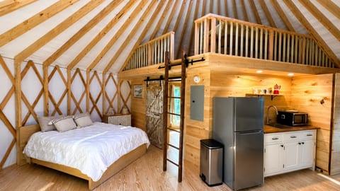 Cozy full-size bed in a luxury yurt with a loft and modern kitchenette.