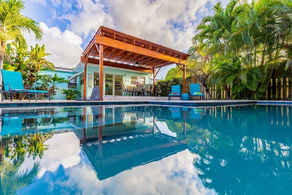 Tropical backyard oasis in Dania Beach with sparkling pool, shaded pergola & sun loungers.