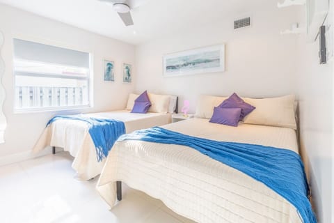 Cozy double-bed room in Dania Beach with cream quilts, blue throws & purple accents.