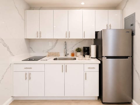 Modern kitchen with white cabinets, marble countertops, stainless steel fridge & coffee maker—fully equipped for your stay.