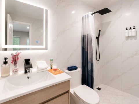 Full bathroom with marble tiles, LED mirror, matte black rain shower & premium toiletries—sleek and modern design.
