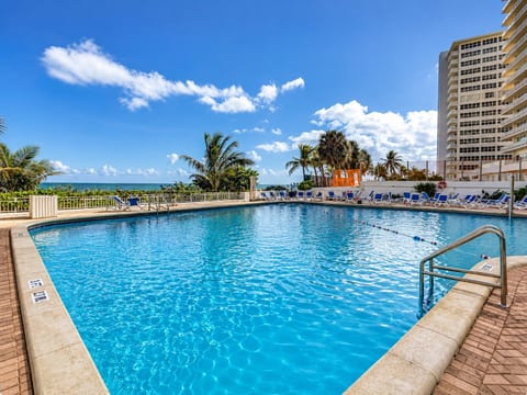 Resort pool with lounge chairs, blue umbrellas, and palm trees—relaxation steps from your condo.