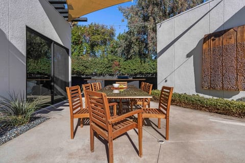 Shaded outdoor dining w/ solid wood table, six chairs & a carved wood door as a backdrop.