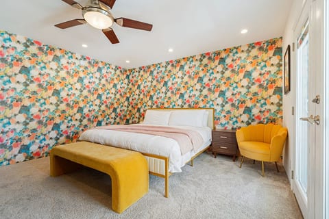 Cheerful bedroom w/ bold wallpaper, cozy bedding, & warm tones that make mornings feel happy.