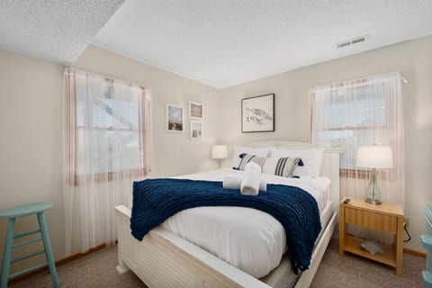 Cozy bedroom w/ soft linens, warm lighting & windows dressed in light curtains