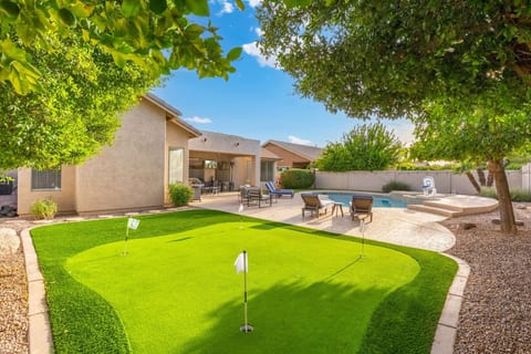 Backyard putting green w/ manicured turf, framed by the pool deck & shaded seating.