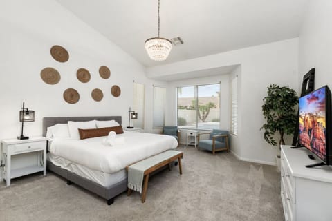 Primary bedroom w/ king bed, woven wall decor, TV & a quiet sitting nook by the window.
