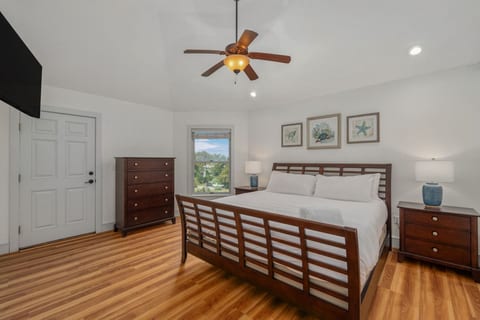 Spacious bedroom w/ a wood-framed bed, hardwood floors & ceiling fan for easy coastal living.