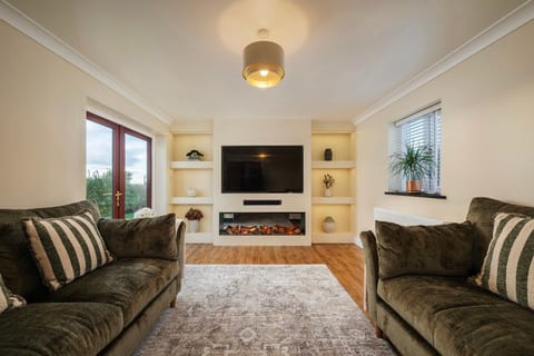 Dual aspect sitting room, patio doors, featuring a media wall with smart LED lighting, 65" smart TV, Sonos sound system and built in electric thermostatic controlled fire.
