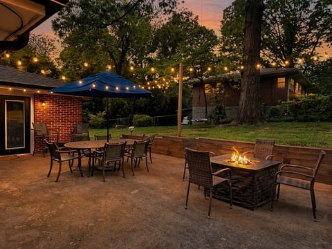 Cozy patio with fire pit, string lights, and dining under the trees