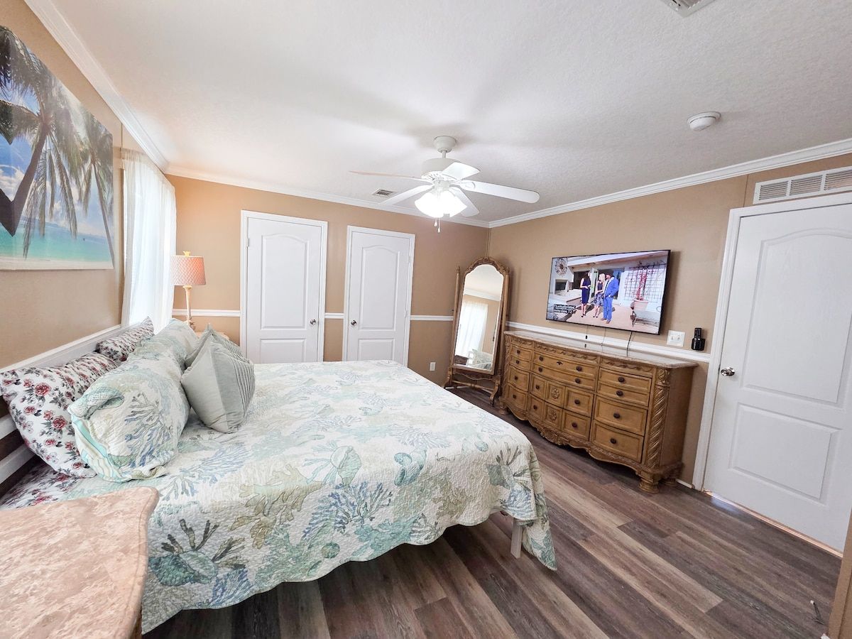 Master Bedroom with King Size Bed, ceiling fan, night stands with lamps and power strips for electronic devices, and a 55" Samsung Smart TV w/ rear LED lighting.