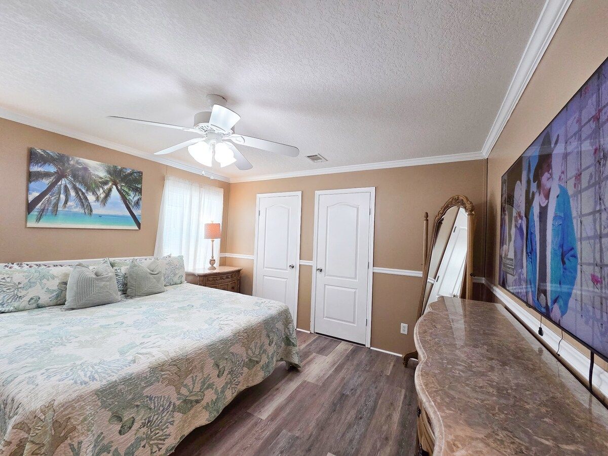 Master Bedroom with King Size Bed, ceiling fan, night stands with lamps and power strips for electronic devices, and a 55" Samsung Smart TV w/ rear LED lighting.