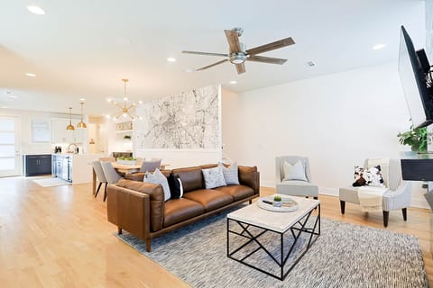Bright and inviting open-concept living space on the main floor, featuring a comfortable leather sofa, stylish accent chairs, a modern coffee table, and a striking wall mural of a Nashville map