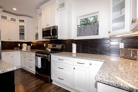 This modern kitchen features crisp white cabinetry, a stylish black backsplash, and a granite island with seating—perfect for breakfast or chatting with the cook.