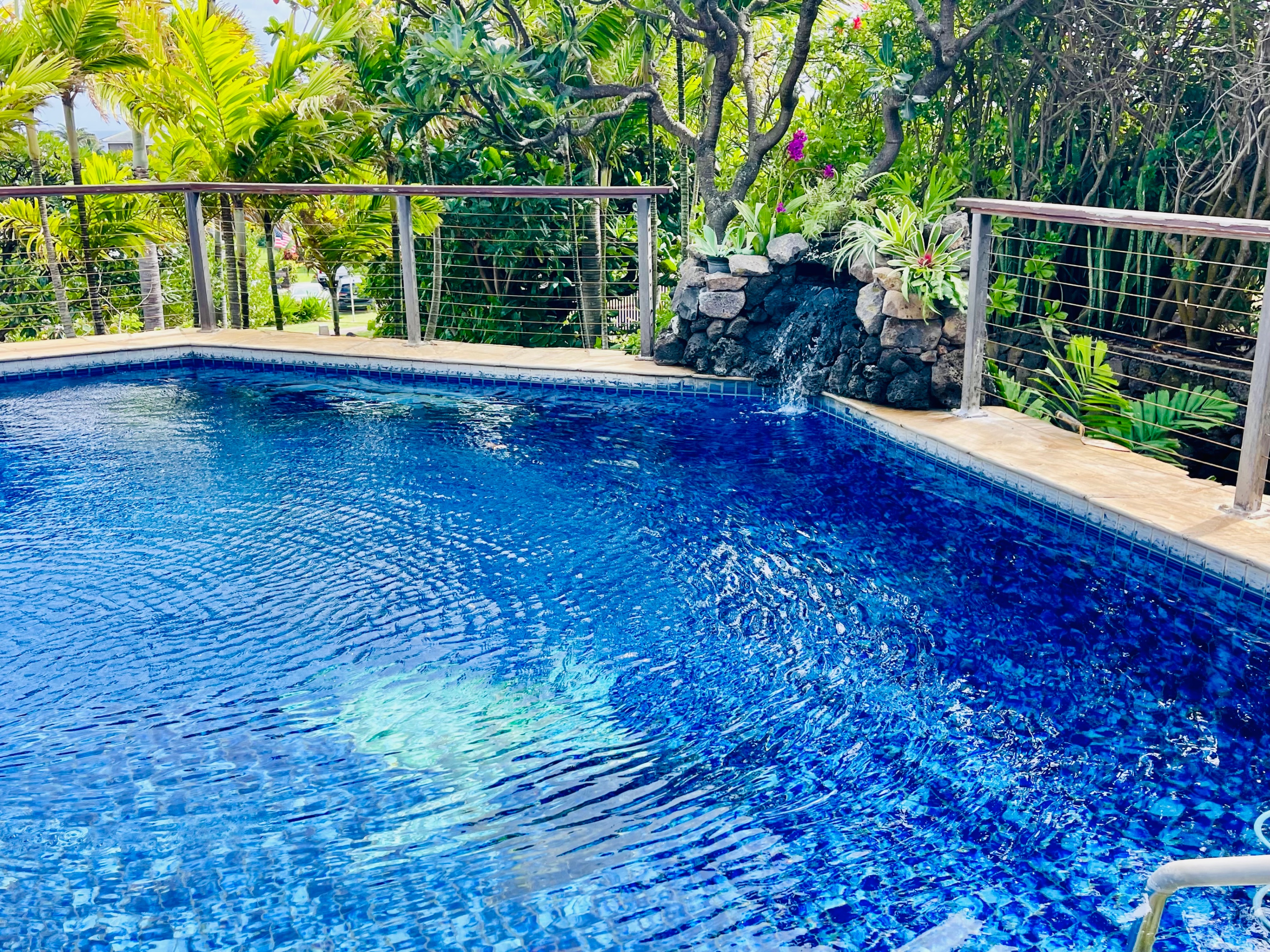 A serene blue-tiled pool surrounded by lush tropical greenery, featuring a small rock waterfall that adds a soothing touch. Perfect for a refreshing swim or peaceful retreat in a private island paradise
