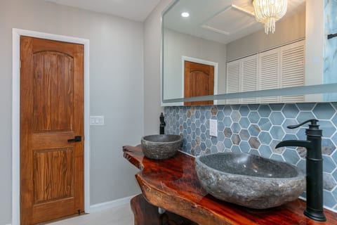 Beautifully renovated bathroom featuring a custom live-edge wood vanity, double stone vessel sinks, elegant lighting, and a spacious walk-in glass shower. A unique spa-inspired space designed for comfort and relaxation.