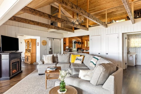 Relax in the spacious, open living area at The Dragonfly Cottage. Featuring a cozy sectional, fireplace, and vaulted ceilings with exposed beams, this room offers both comfort and charm—perfect for unwinding after a day by the lake.