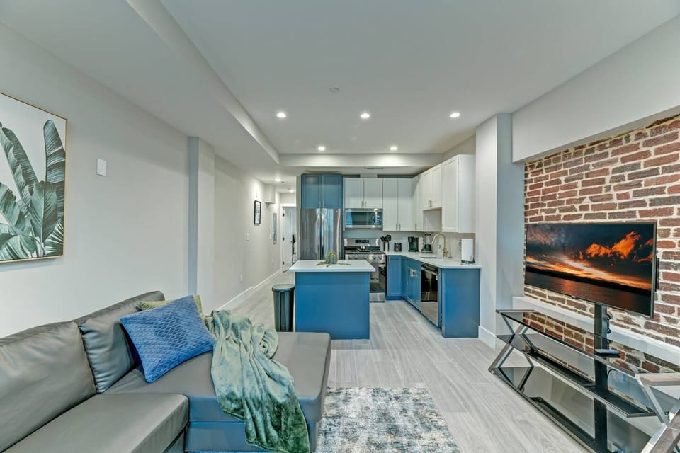 Modern Comfort Meets Historic Charm: Relax in this beautifully designed living space, featuring a sleek kitchen, cozy sectional, and exposed brick accents for the perfect blend of style and warmth.
