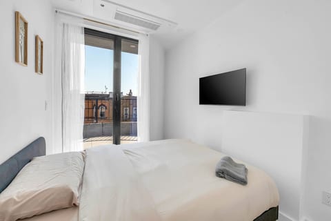 Bright bedroom with crisp white linens, a wall-mounted TV and balcony access — wake up to natural light.