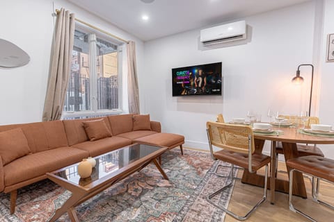 Cozy living + dining zone with a plush sectional, smart TV, and A/C—ideal for movie nights and meals at home. Big windows bring in natural light, while the warm textures and table set for four make it easy to gather and relax