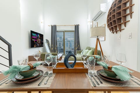 Bright living room with smart TV, green sofa and floor‑to‑ceiling windows overlooking street.