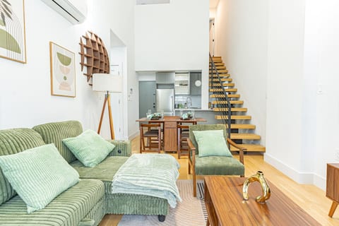 Mid‑century modern living area with green sofa, wood accents and staircase in Bushwick penthouse.