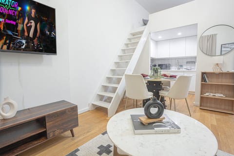 Bright open-plan living space featuring a cozy lounge with smart TV, a modern dining area, and a fully equipped kitchen. A stylish staircase leads to the loft, adding extra charm and functionality