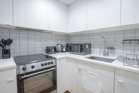 Fully equipped modern kitchen featuring stainless steel appliances, a sleek stovetop oven, microwave, coffee maker, toaster, and electric kettle. The clean tile backsplash and ample cabinetry provide both style and convenience