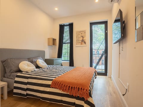 Bright bedroom with balcony access, comfy bed, modern comforts and breezy views of Brooklyn.