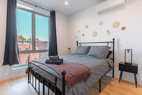 Queen bedroom with plush linens, modern décor and large windows overlooking Brooklyn streets.