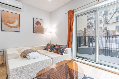Modern living room with a white couch, orange curtains, wall art, floor lamp and a glass door to a balcony