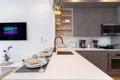 Eat-in kitchen island set for dining — sleek quartz counter, pendant lighting, and full cookware in this renovated Brooklyn duplex.