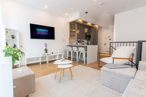 Sunlit open-plan living room with a plush sectional, smart TV, and seamless flow to the kitchen — the heart of this spacious renovated Brooklyn duplex.