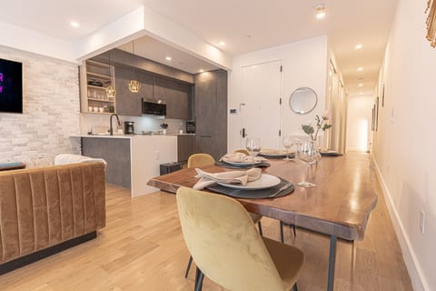 Sunlit dining area with a real wood table and cushioned banquette, flowing into the kitchen — gather and dine in comfort.