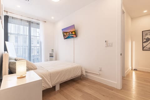 Bright, restful bedroom with big windows, a comfy bed and wall-mounted TV — quiet, comfortable nights in Brooklyn.
