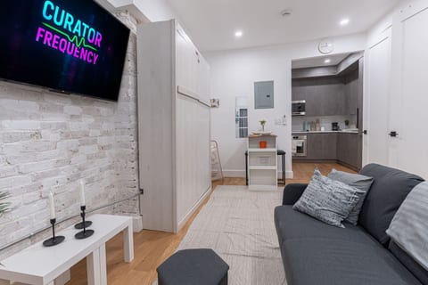 Cozy living space with smart TV, comfy seating and exposed brick, opening to the kitchen — a warm, modern Brooklyn hideaway.