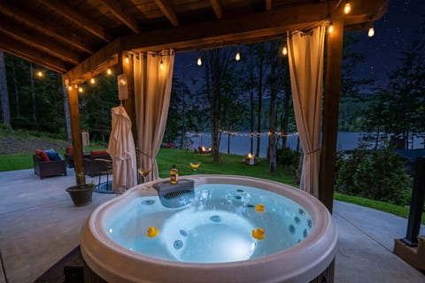 Private lakeside hot tub with string lights and serene evening views