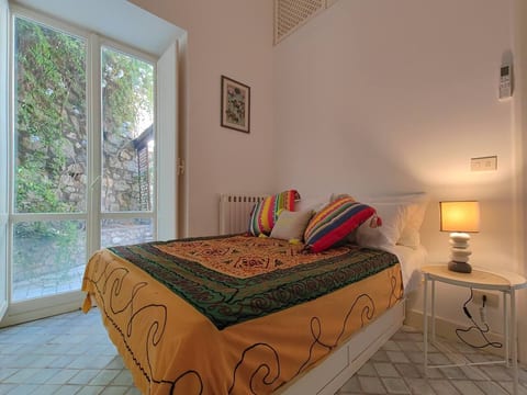A charming and tranquil bedroom featuring colorful textiles, soft lighting, and large glass doors that open to a lush garden retreat.