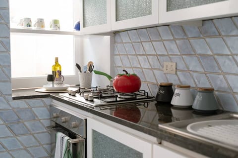 A bright and charming kitchen featuring modern cabinetry, a geometric tiled backsplash, and a bold red kettle that adds a touch of color and warmth