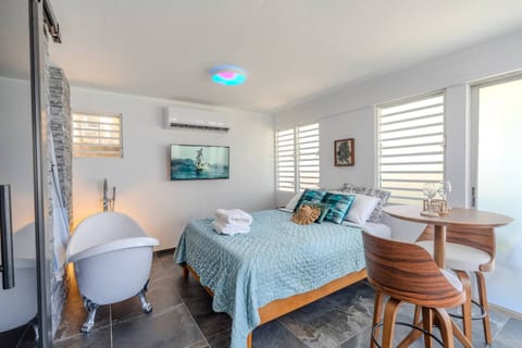 A modern, sunlit space featuring a comfy bed, elegant tub, and a cozy dining nook easy to settle right in.