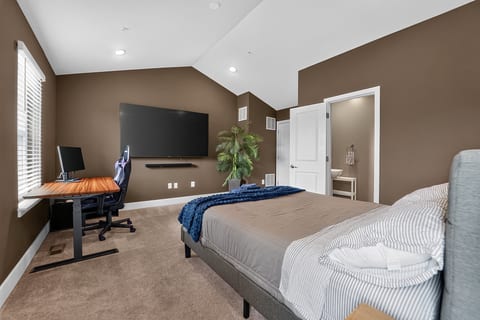 Spacious bedroom with vaulted ceilings, workspace, and large TV