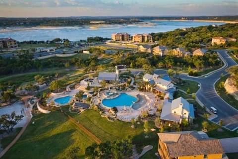 Aerial view of the resort-style community of The Hollows, near Lake Travis, with pools, green space, and scenic Hill Country surroundings